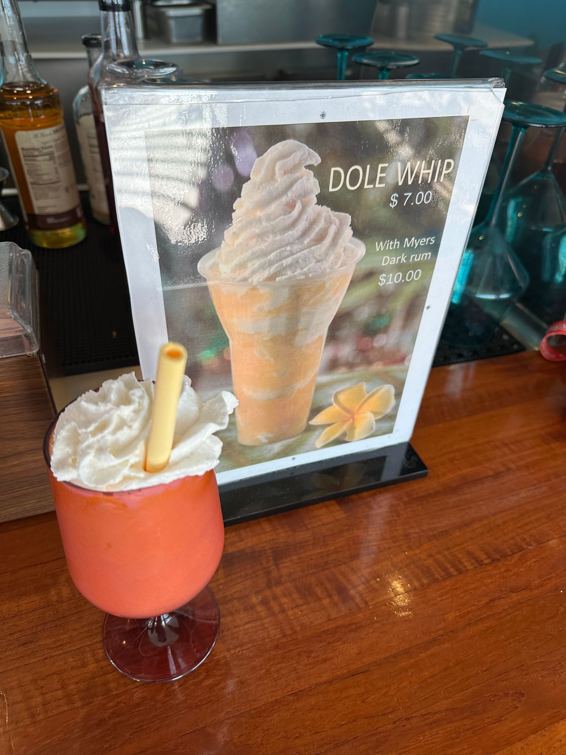 Cocktail on bar with menu sign for Dole Whip, orange and white colors.