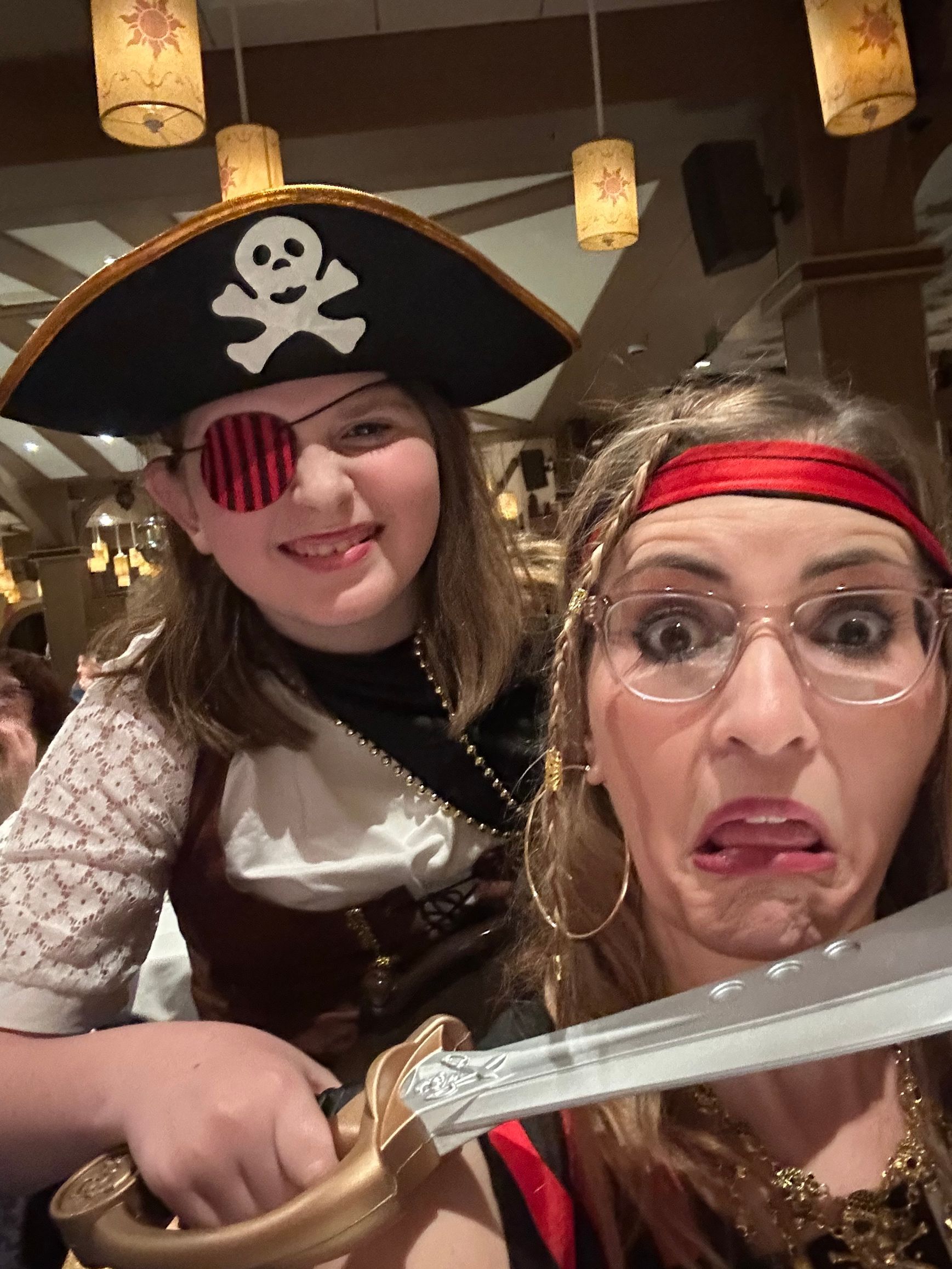 A girl and woman in pirate costumes pose with a toy sword; the woman makes a silly face.