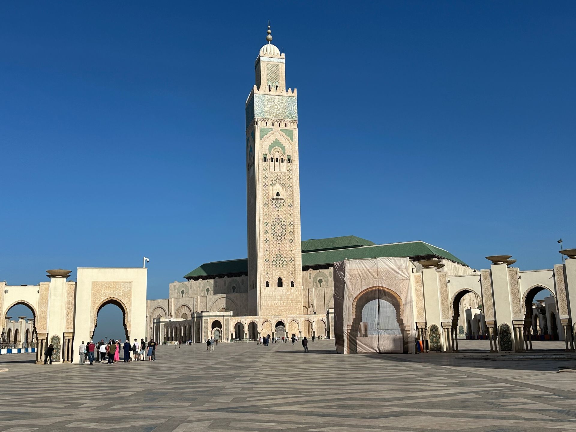 Hassan II Mosque in Casablanca, Morocco; tall minaret, arches, and large courtyard; blue sky.