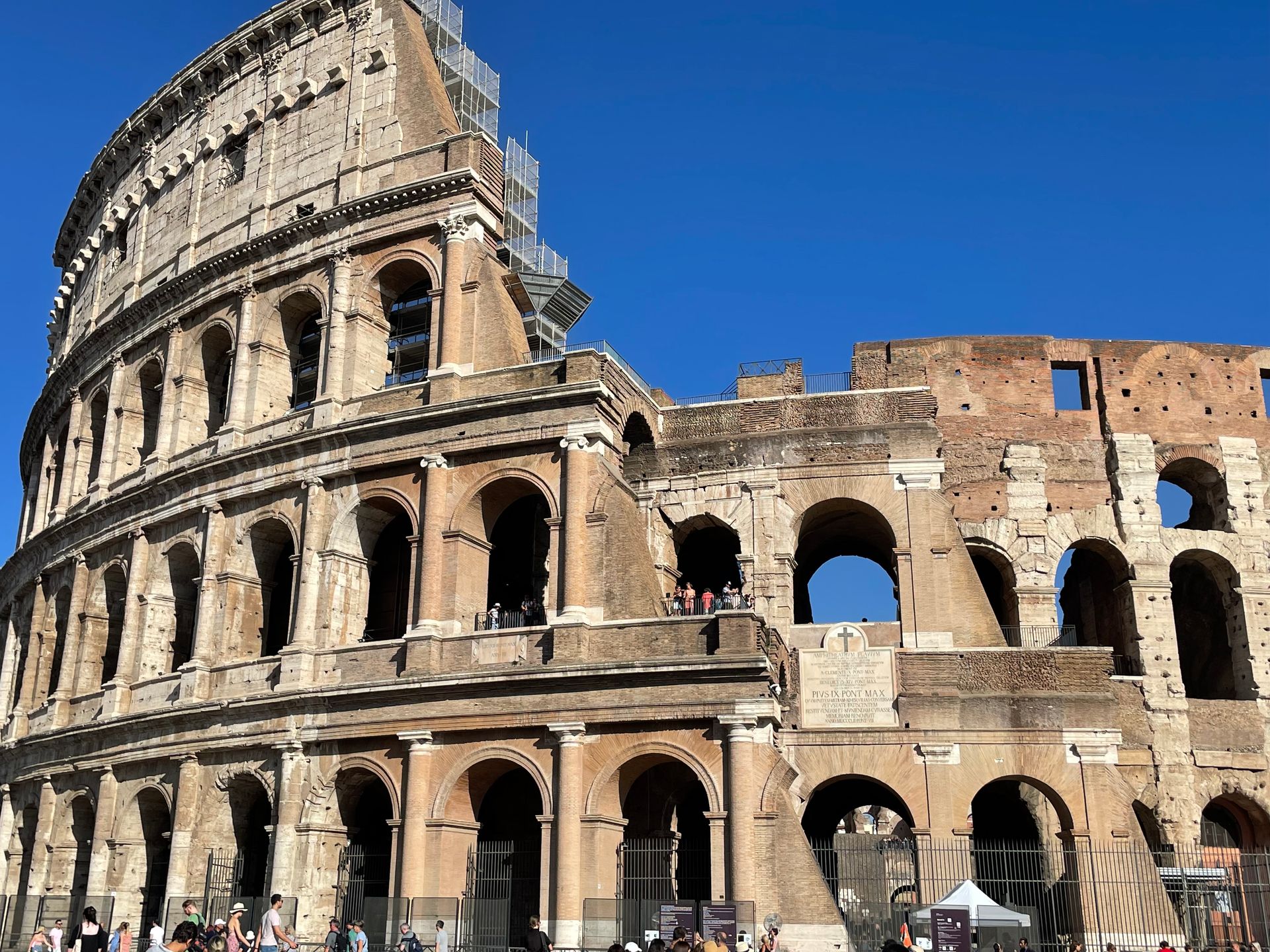 The Colosseum in Rome, Italy, a large stone amphitheater with arched openings under a bright blue sky.