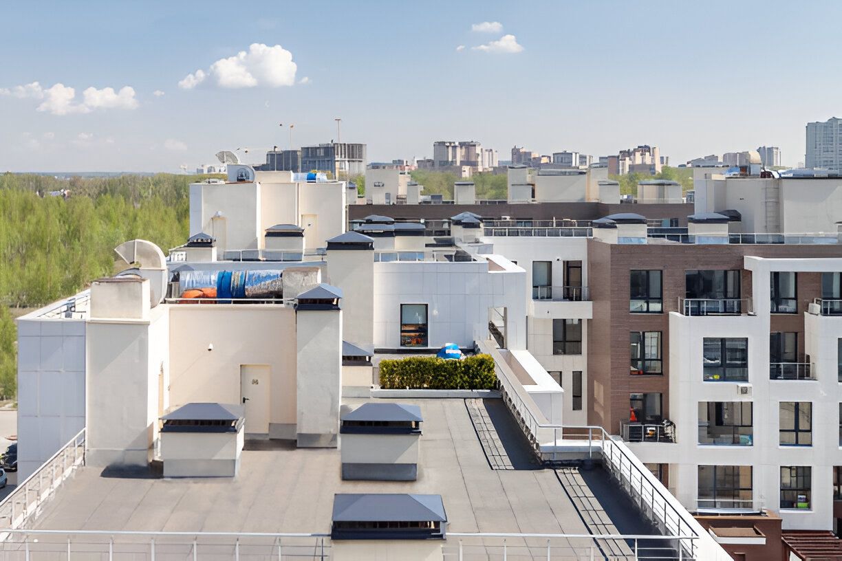 Rooftop view of apartment buildings with chimneys and green rooftop garden on a sunny day.