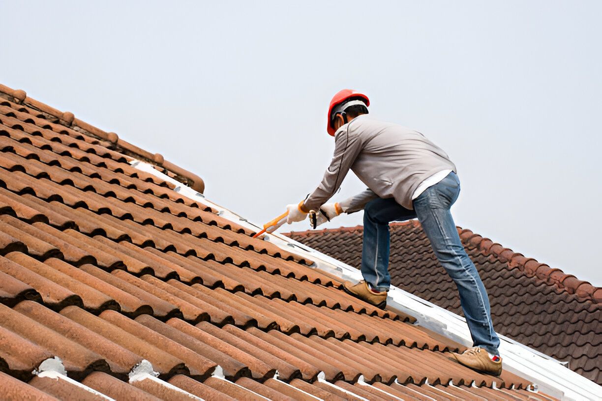 Roofer in an orange hard hat applies caulk to the tiles on a rooftop.