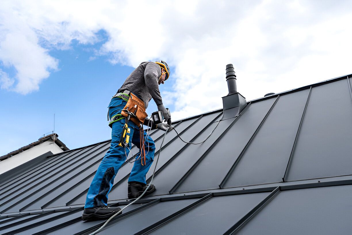 Roofer in safety harness working on a metal roof under a partly cloudy blue sky.