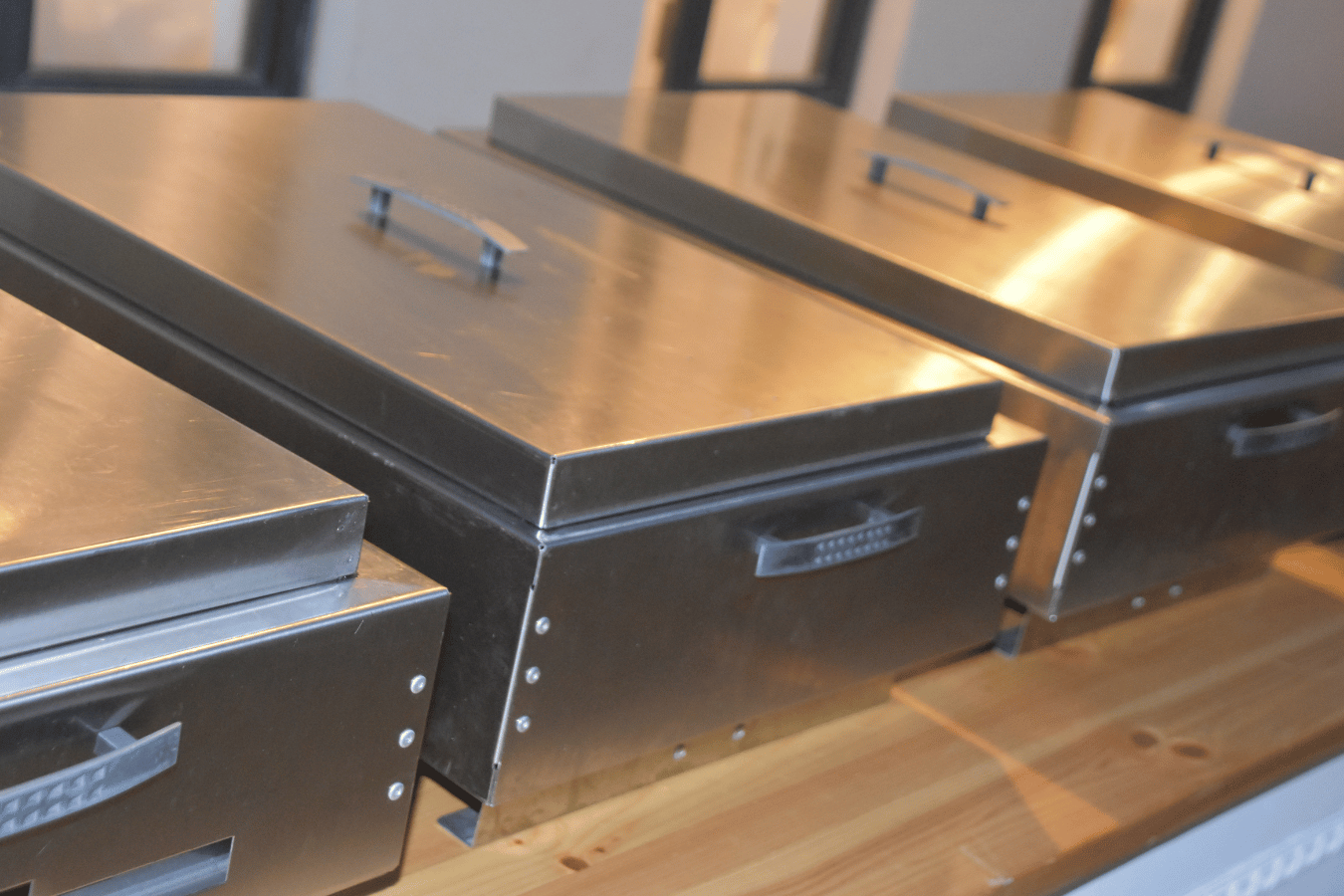 A row of stainless steel boxes with handles on a wooden table