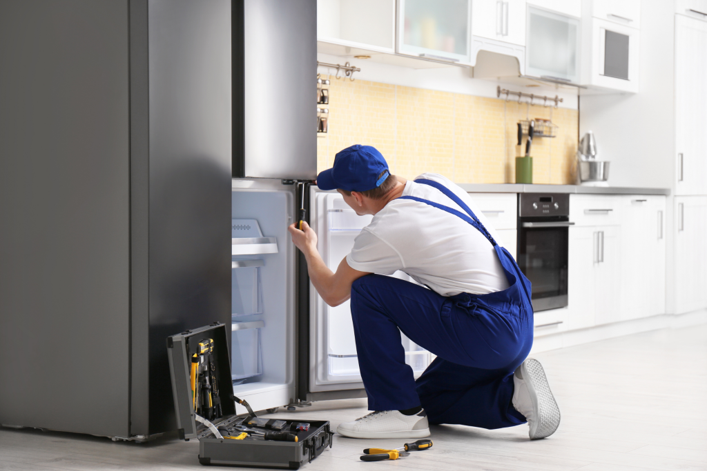Male Technician with Screwdriver Repairing Refrigerator in Kitchen