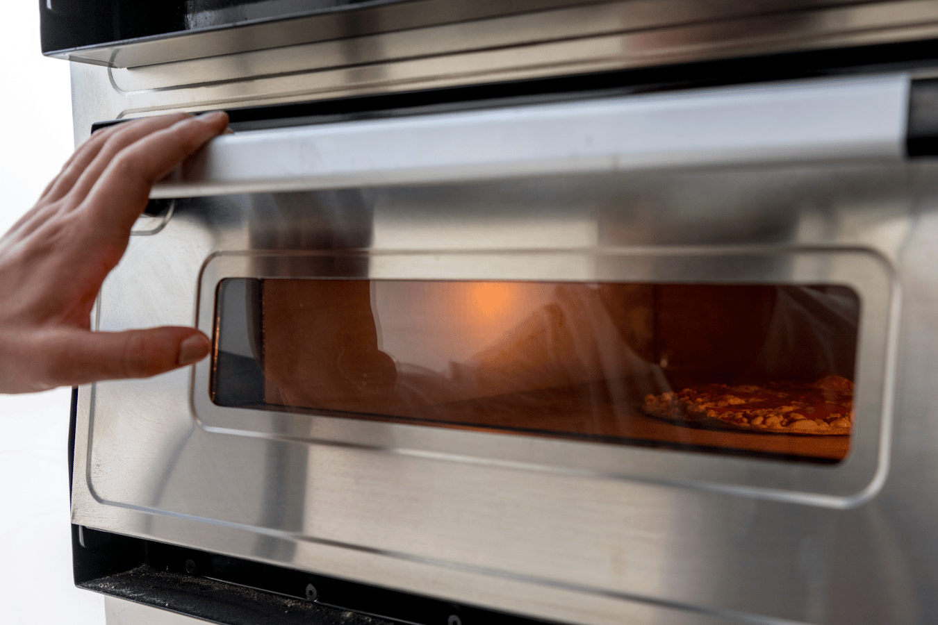 A person is opening the door of a stainless steel oven.