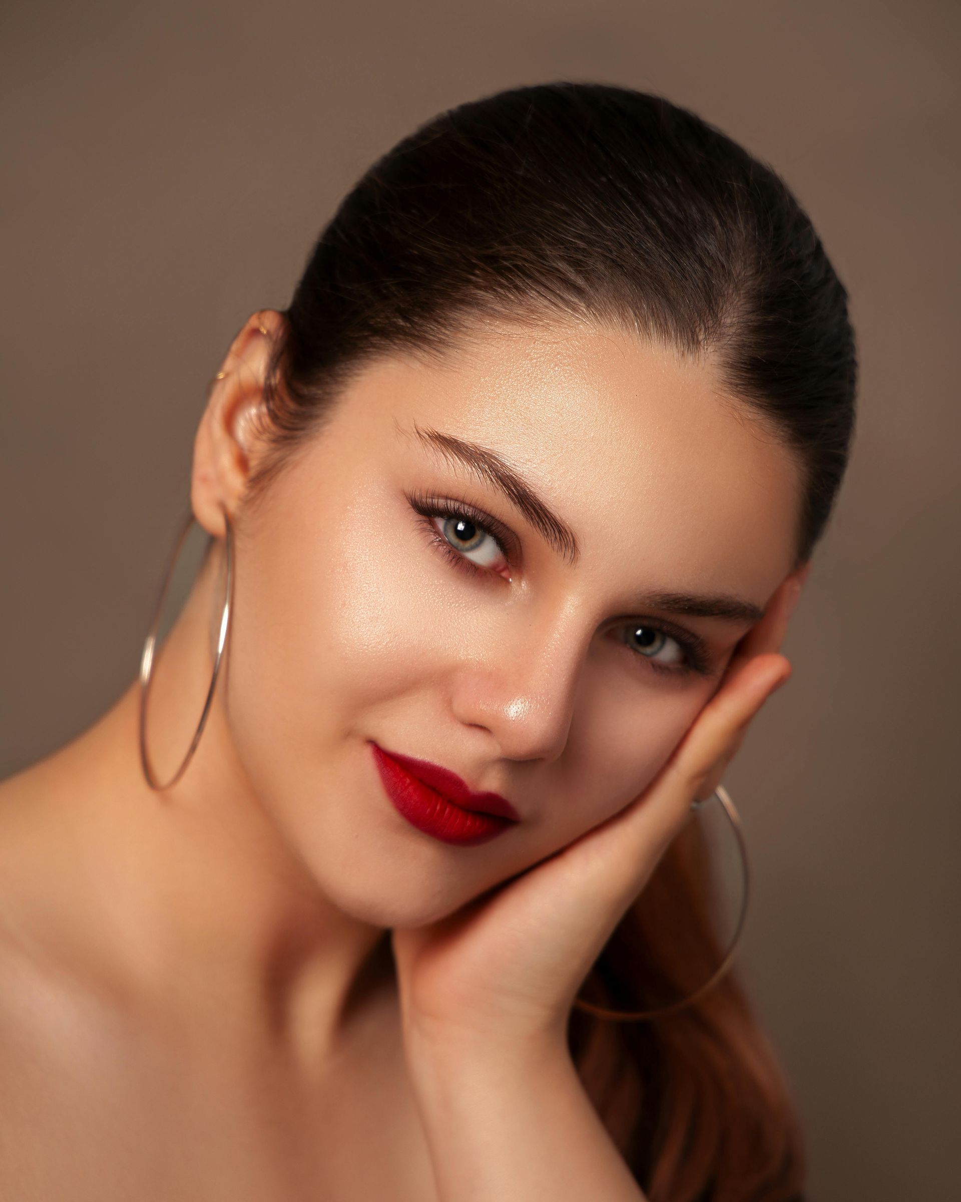 Woman with red lipstick and glitter makeup, resting her head on her hand.