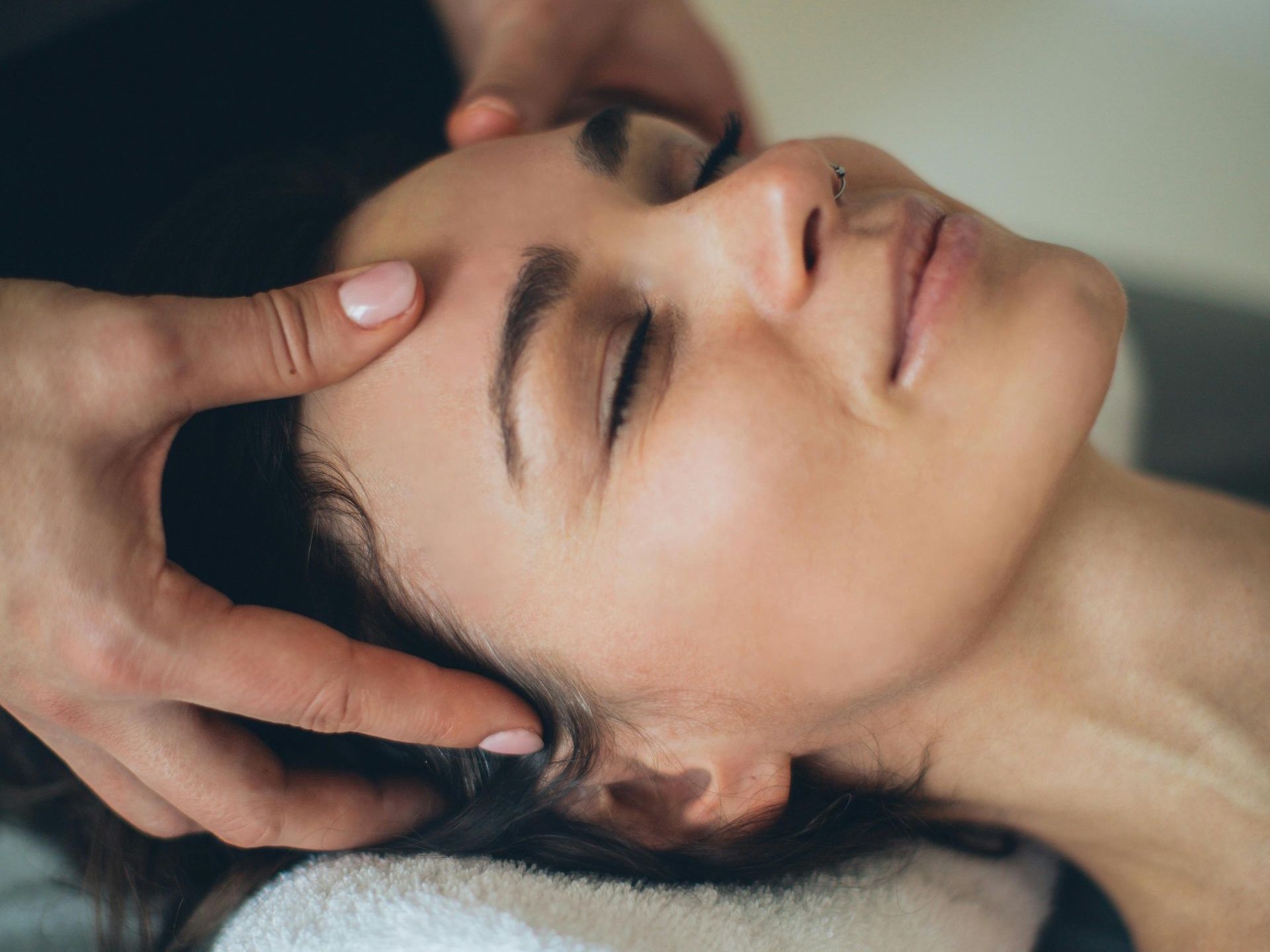 Woman receiving a head massage, eyes closed, hands on her forehead.