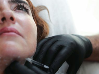 Woman receiving an injection in her jaw from a gloved hand in a clinical setting.