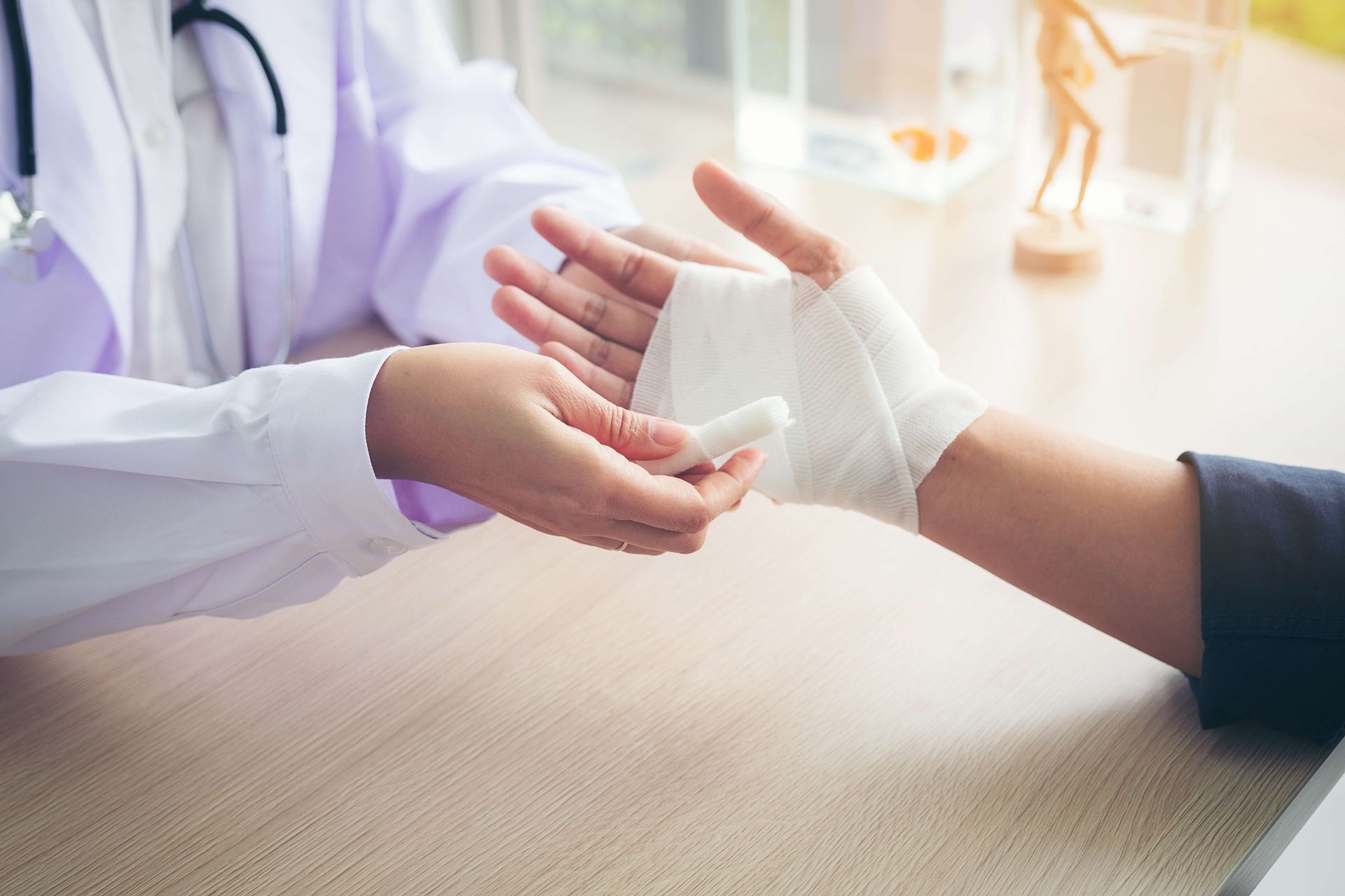 Doctor wrapping a patient's injured hand with a bandage in a well-lit medical office.