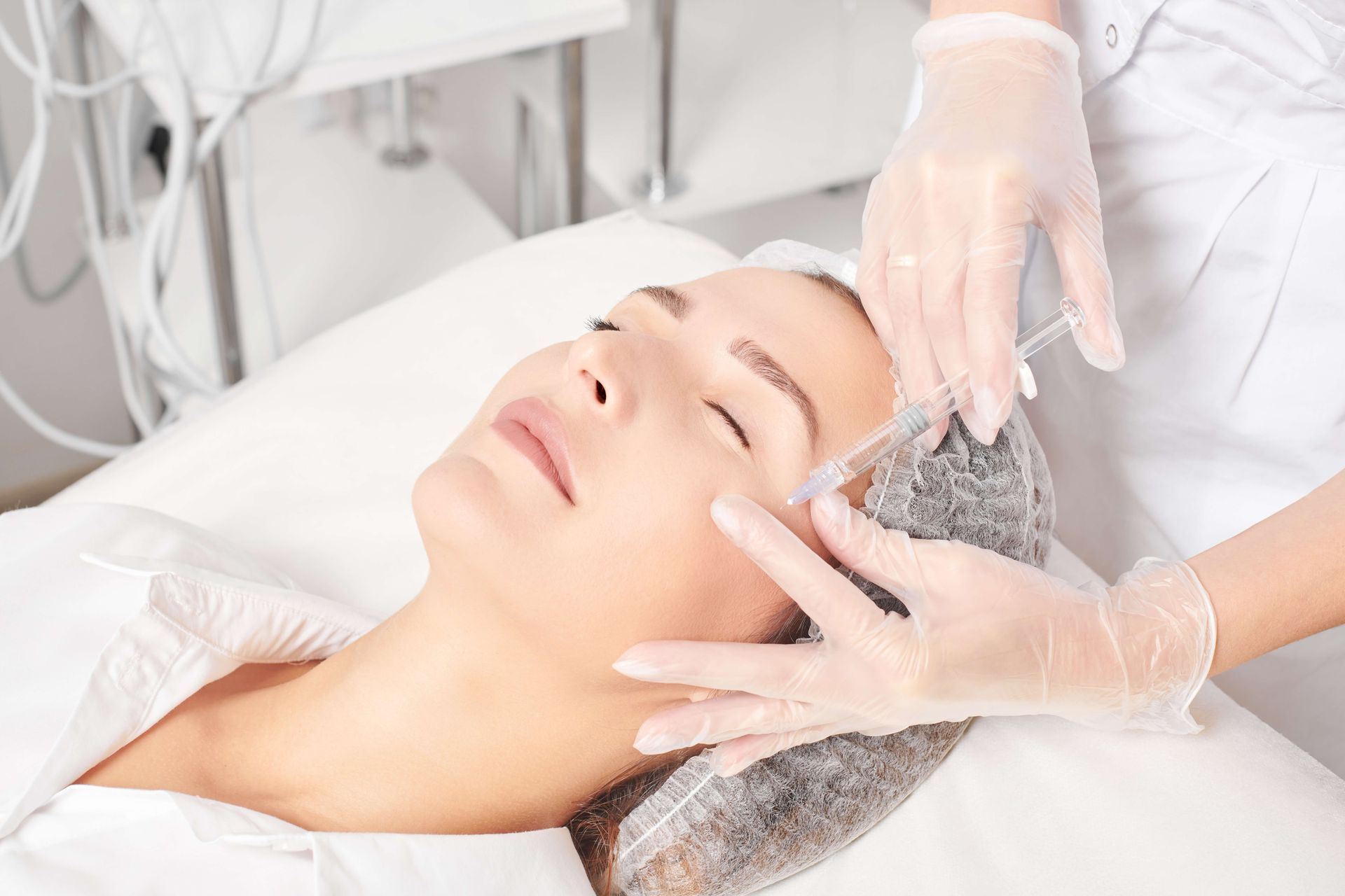 A person receiving a facial injection from gloved hands; close-up, indoors.