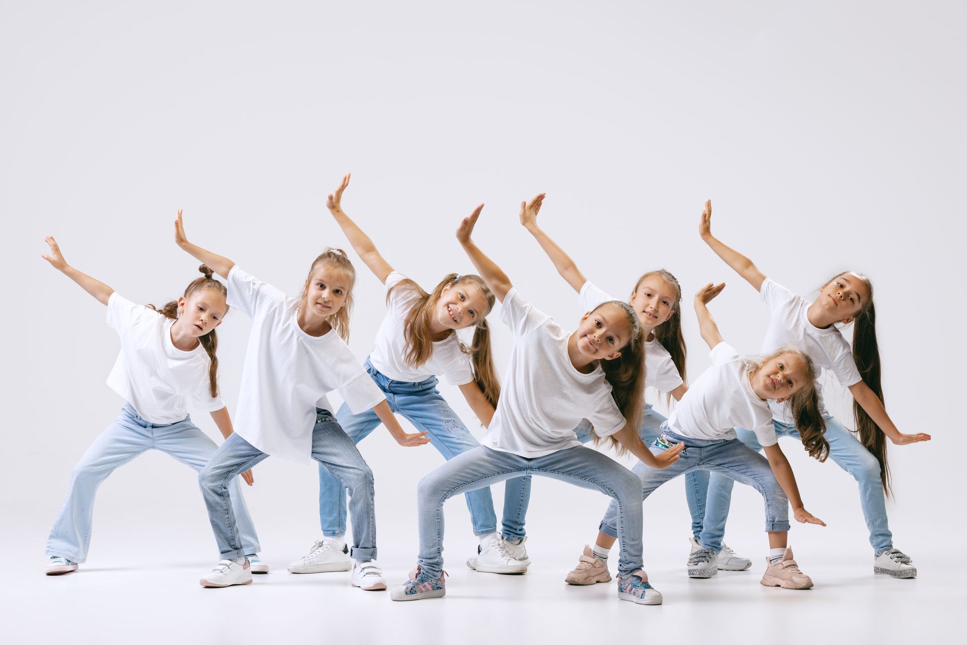 Group of young girls in white shirts and jeans, dancing against a white background.