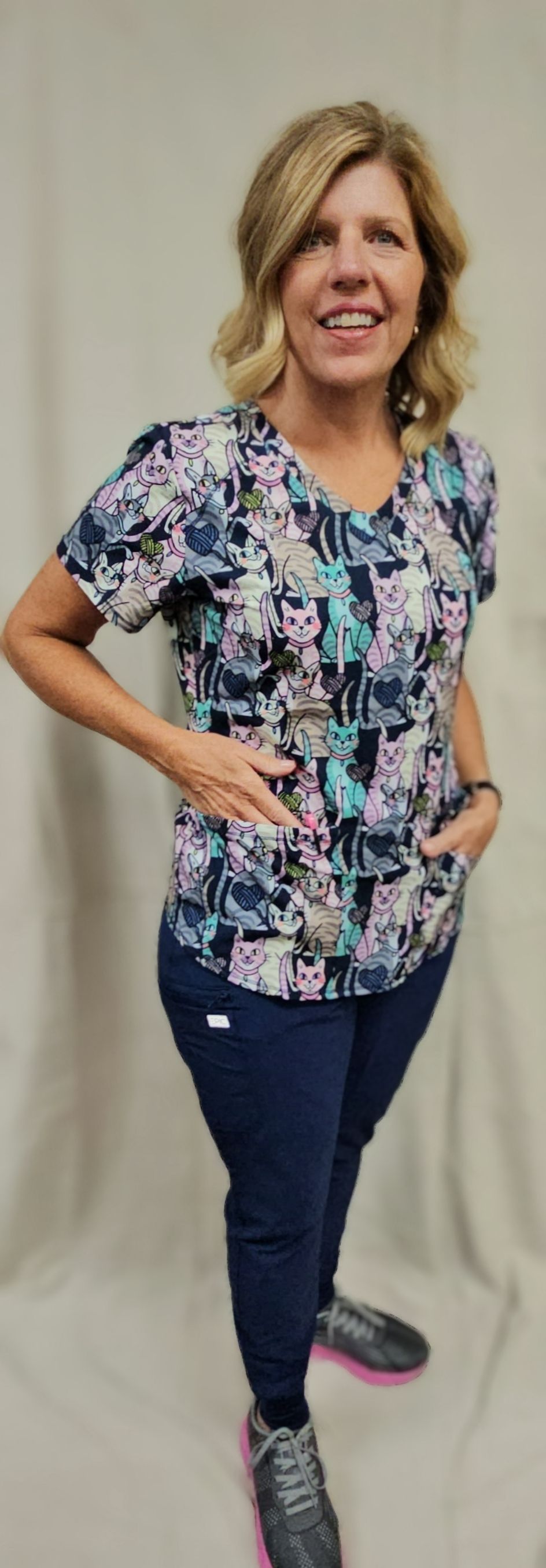 A woman in a scrub top and pants is standing with her hands in her pockets.