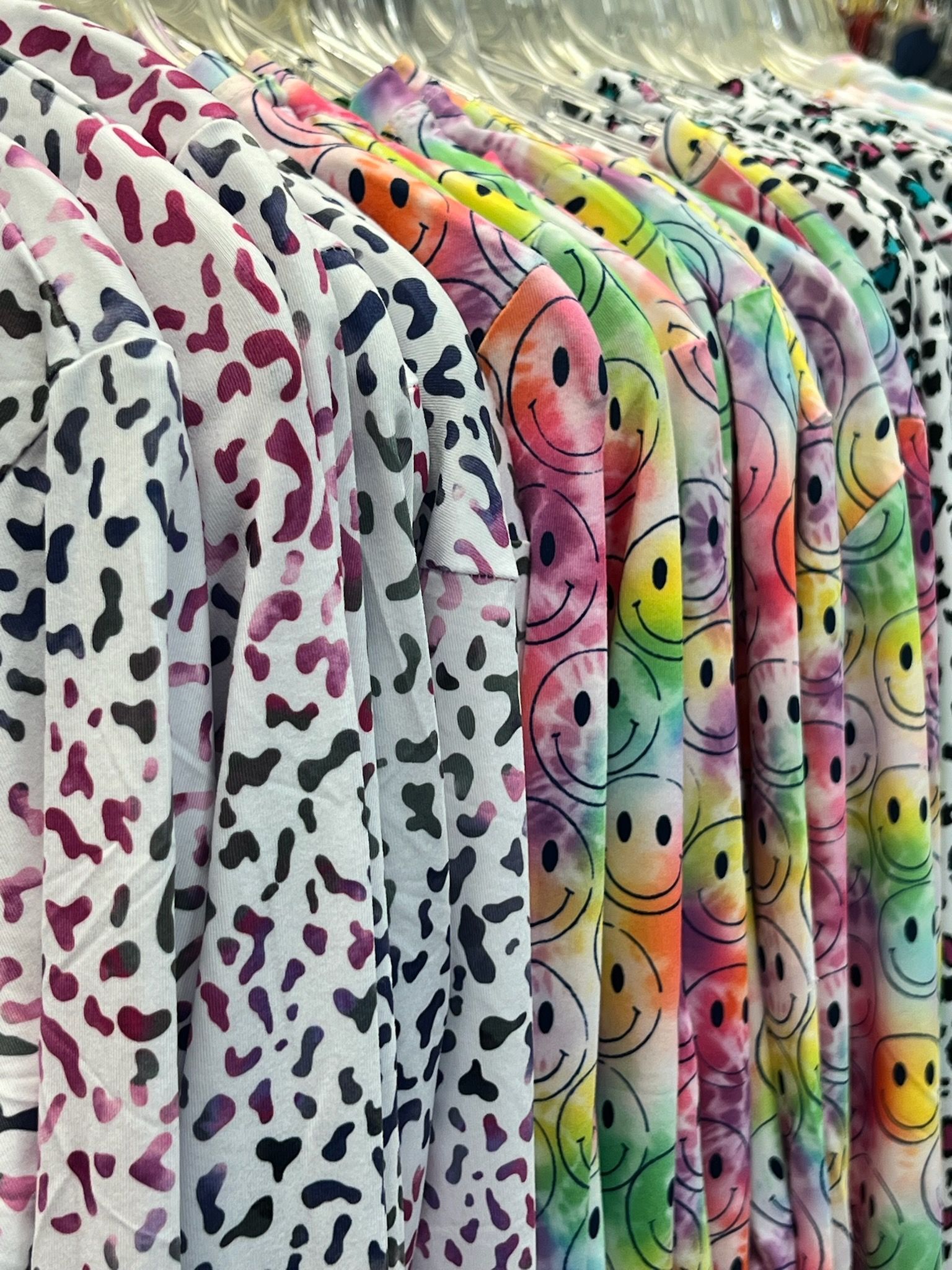 A row of colorful shirts with smiley faces on them are hanging on a rack.