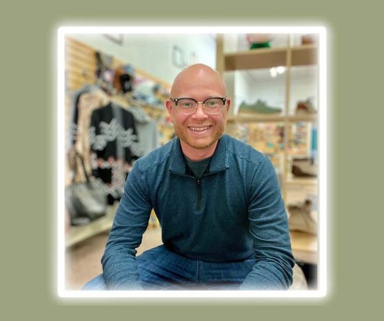 A man wearing glasses and a blue shirt is sitting in a store.