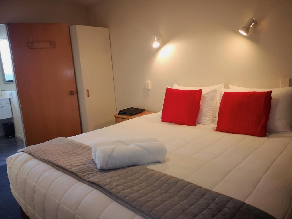 A hotel room with a king size bed and red pillows.