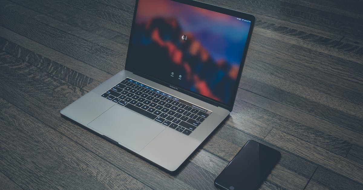 A laptop computer is sitting on a wooden floor next to a cell phone.