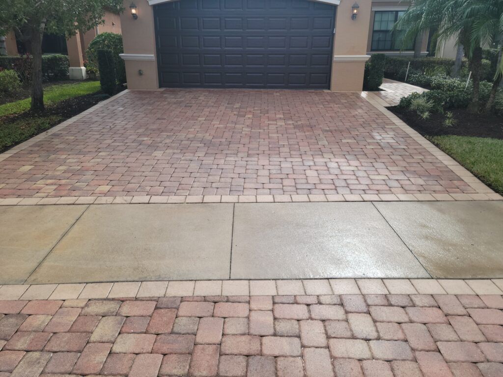 Brick driveway and sidewalk leading to a dark garage door of a house.
