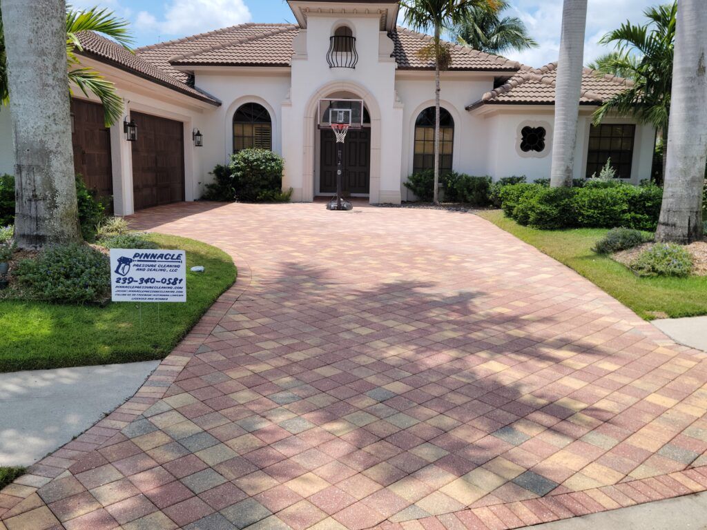 A brick driveway leads to a white house with a basketball hoop.