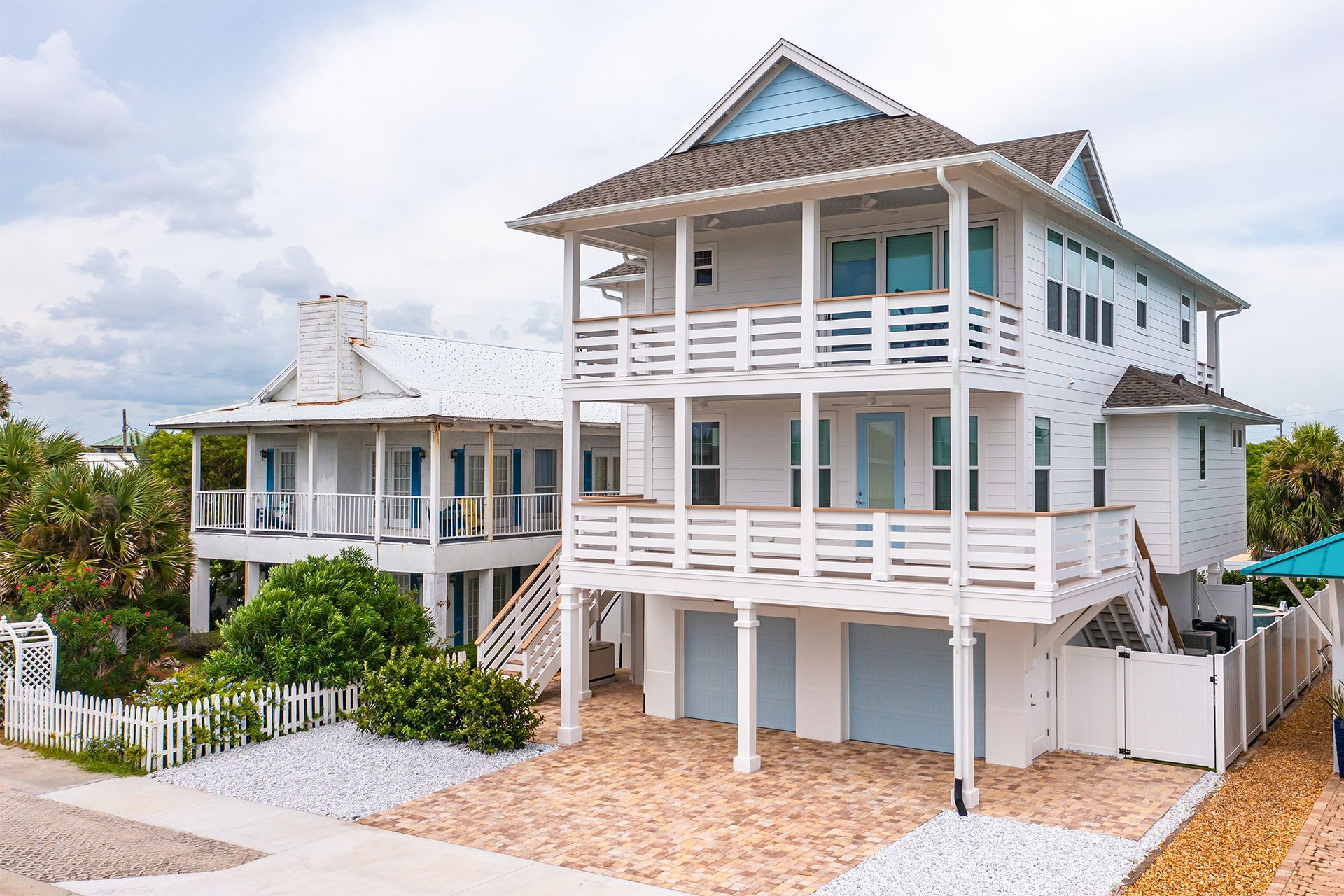 Two white beach houses with balconies and pavers driveway.