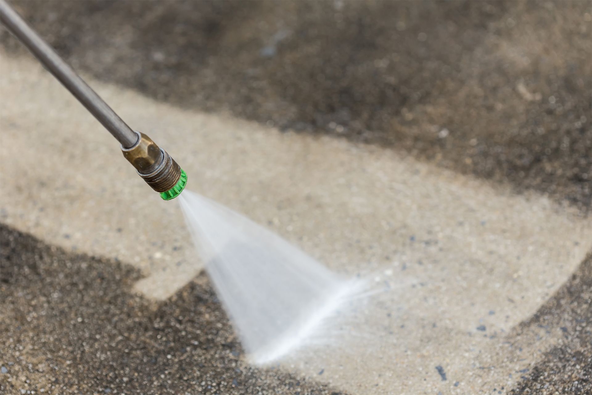 A pressure washer spraying water onto a concrete surface, cleaning a light-colored strip.