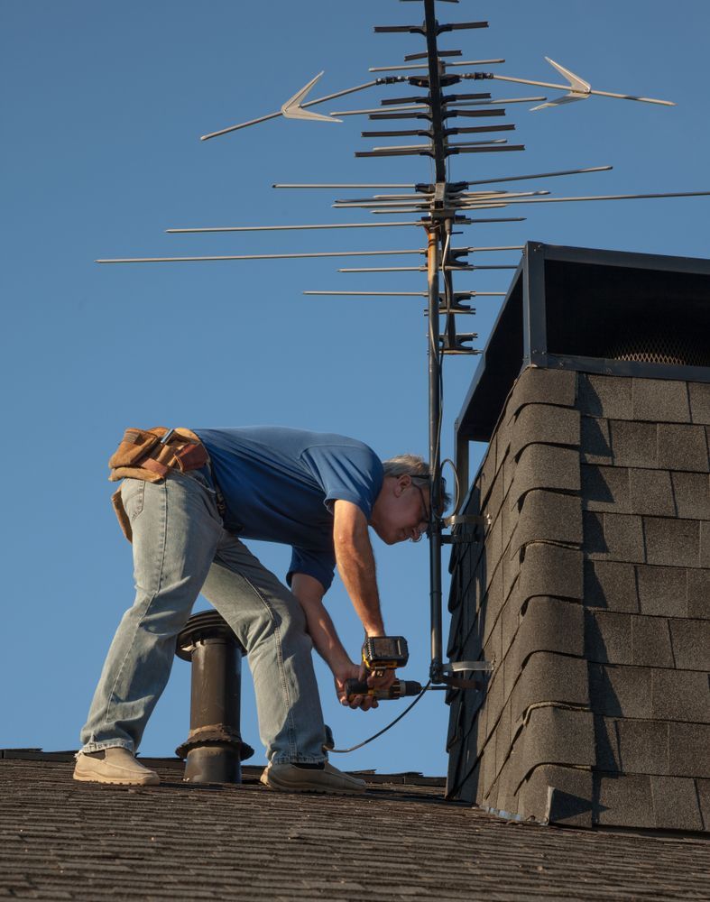 A man is working on a roof with an antenna in the background.