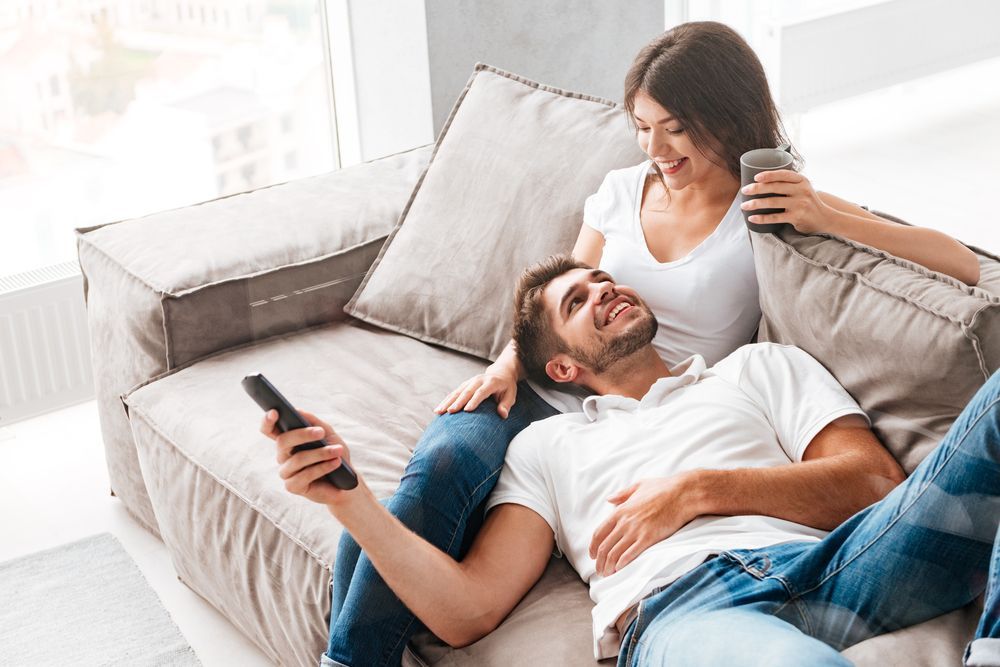 A man and a woman are sitting on a couch while holding a remote control.