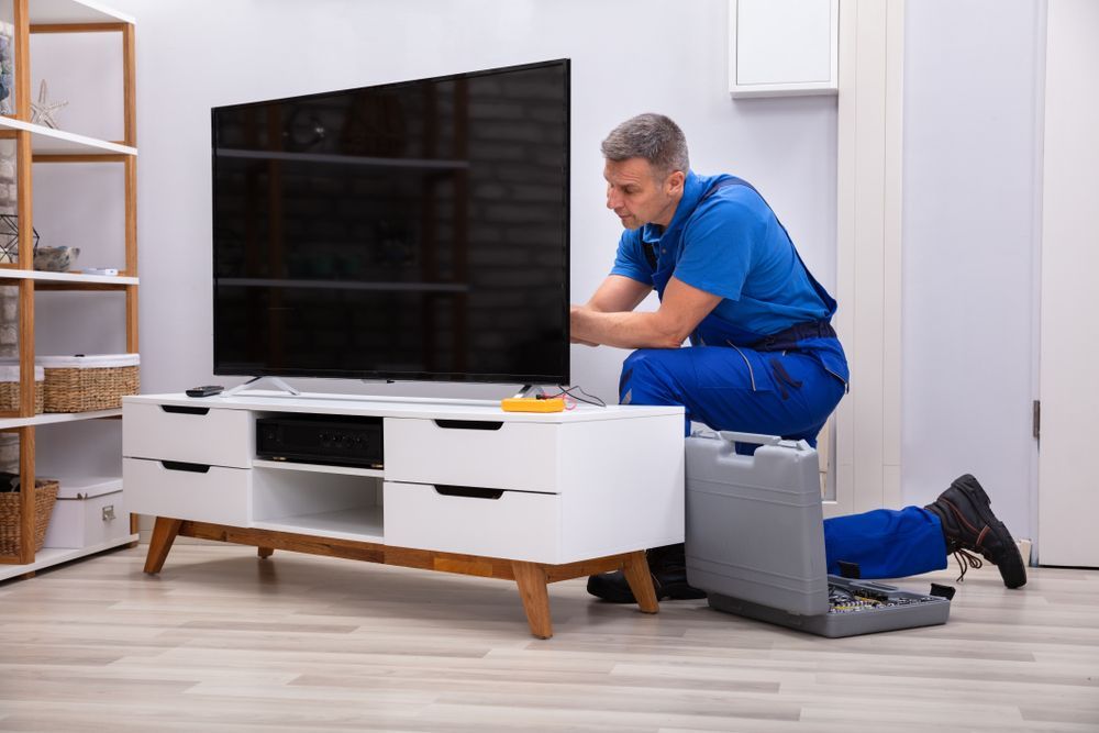 A man is fixing a flat screen tv on a stand in a living room.