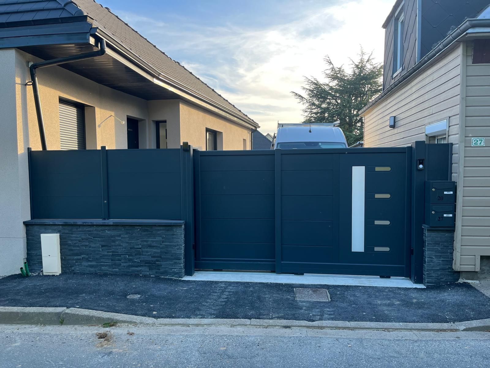 Portail d'allée moderne noir avec lattes verticales en bois, adossé à une maison au toit gris.