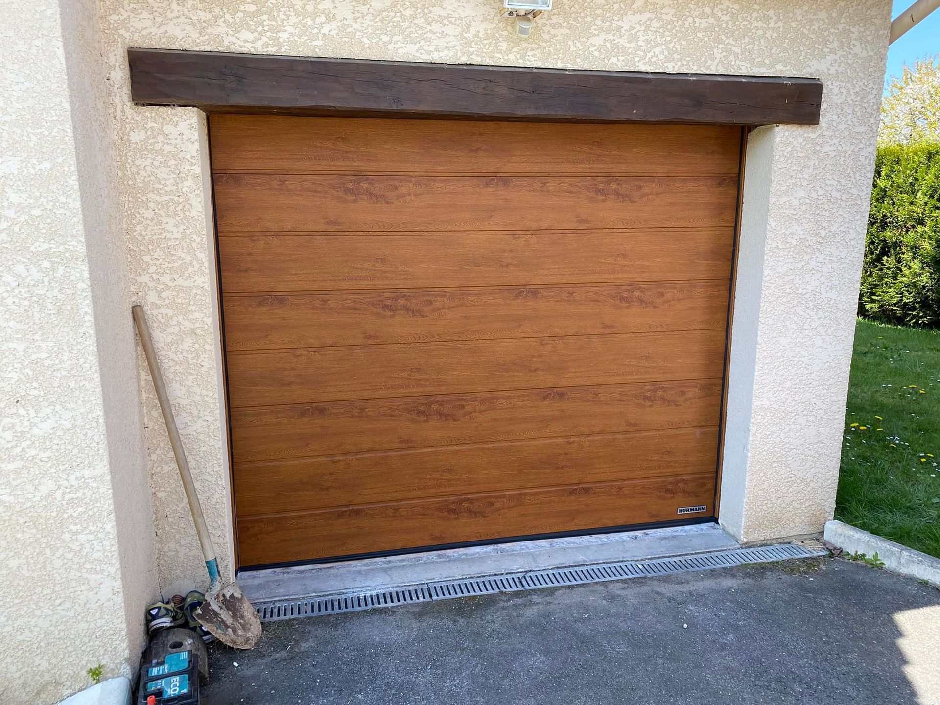 Porte de garage gris foncé sur un bâtiment de couleur claire, allée pavée et buissons verts devant.