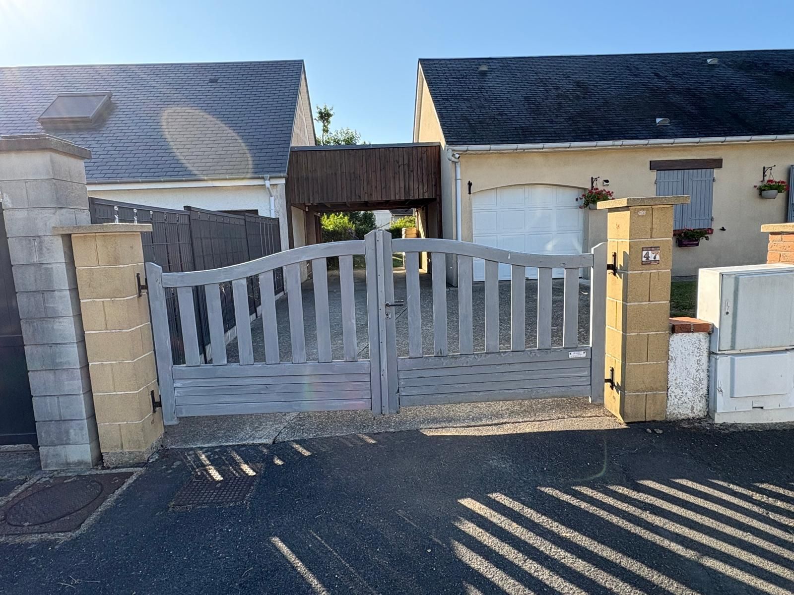 Portail en bois gris devant deux bâtiments. Le portail est fermé, avec le numéro 3 de la maison sur le pilier de droite.