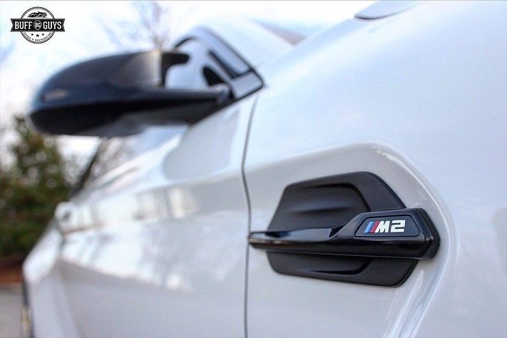 White BMW M2 car door handle with M badge and black side mirror.