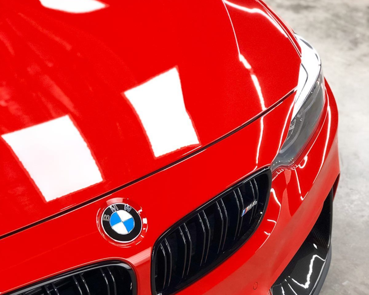 Bright red BMW car front with black grille and logo reflecting light.