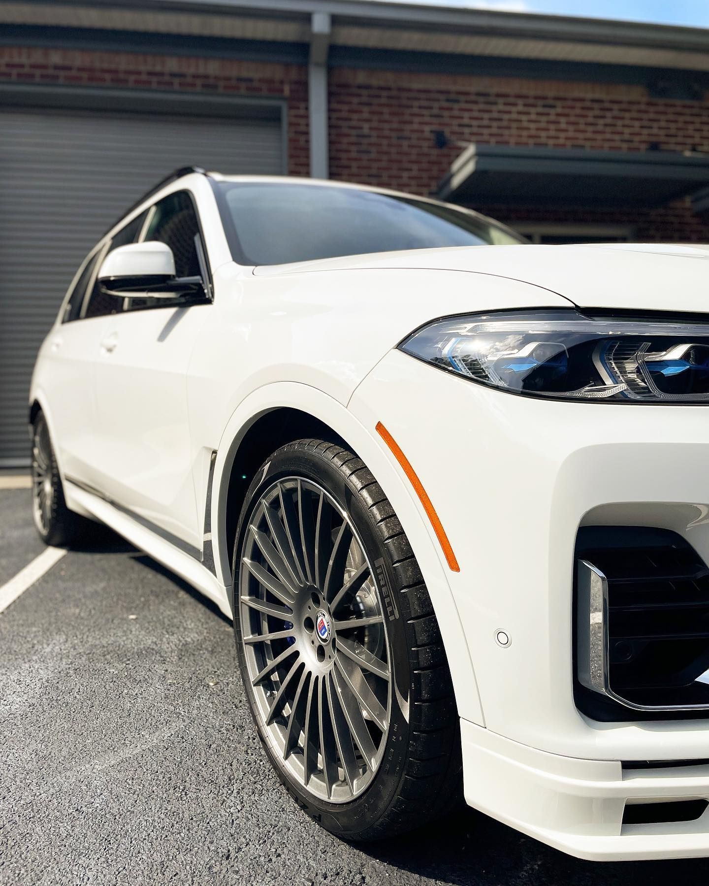 White BMW SUV parked next to a brick building, close-up of front with a custom rim and tire.