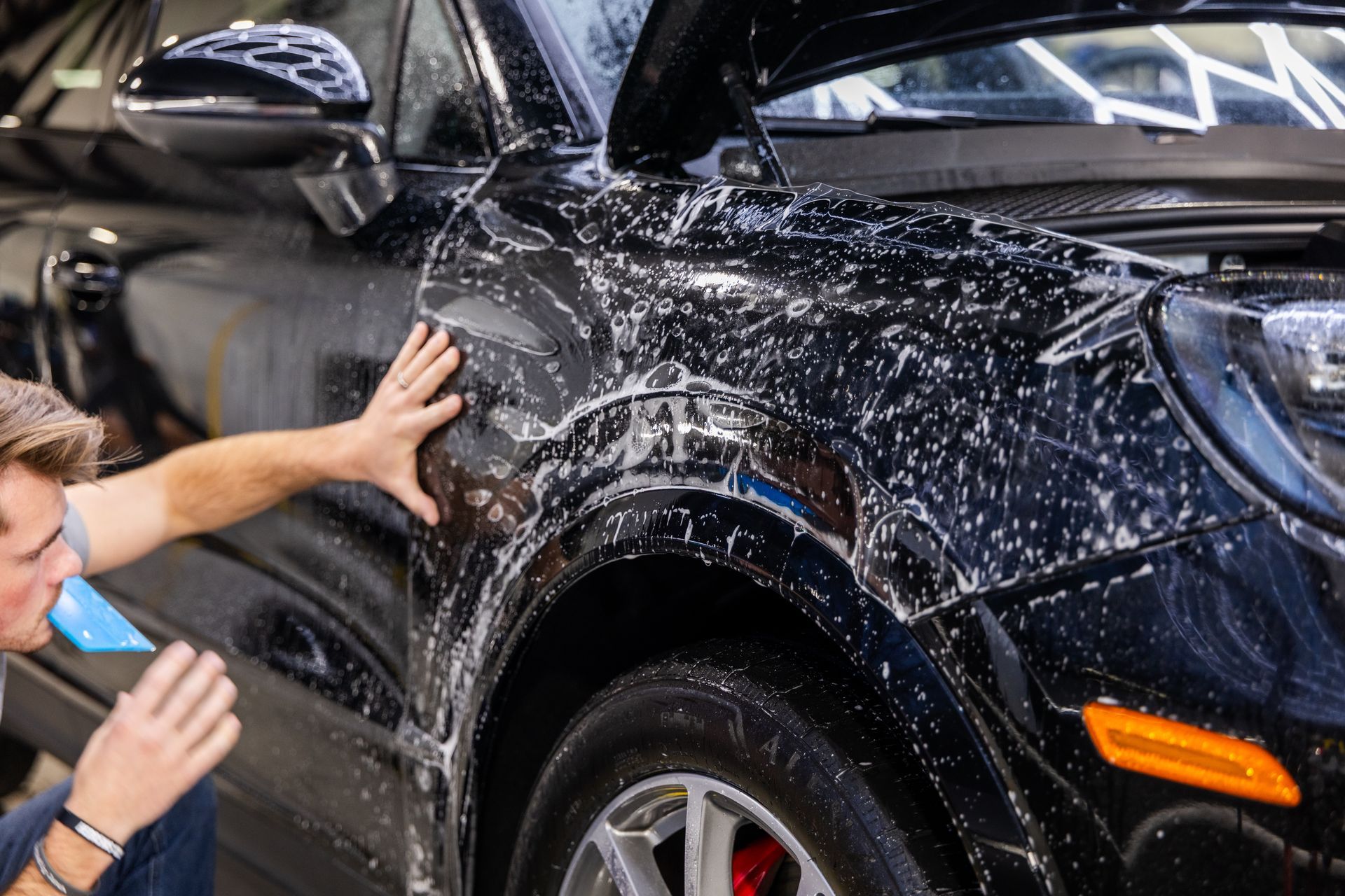 Man washing a black car with soapy water, outdoors.