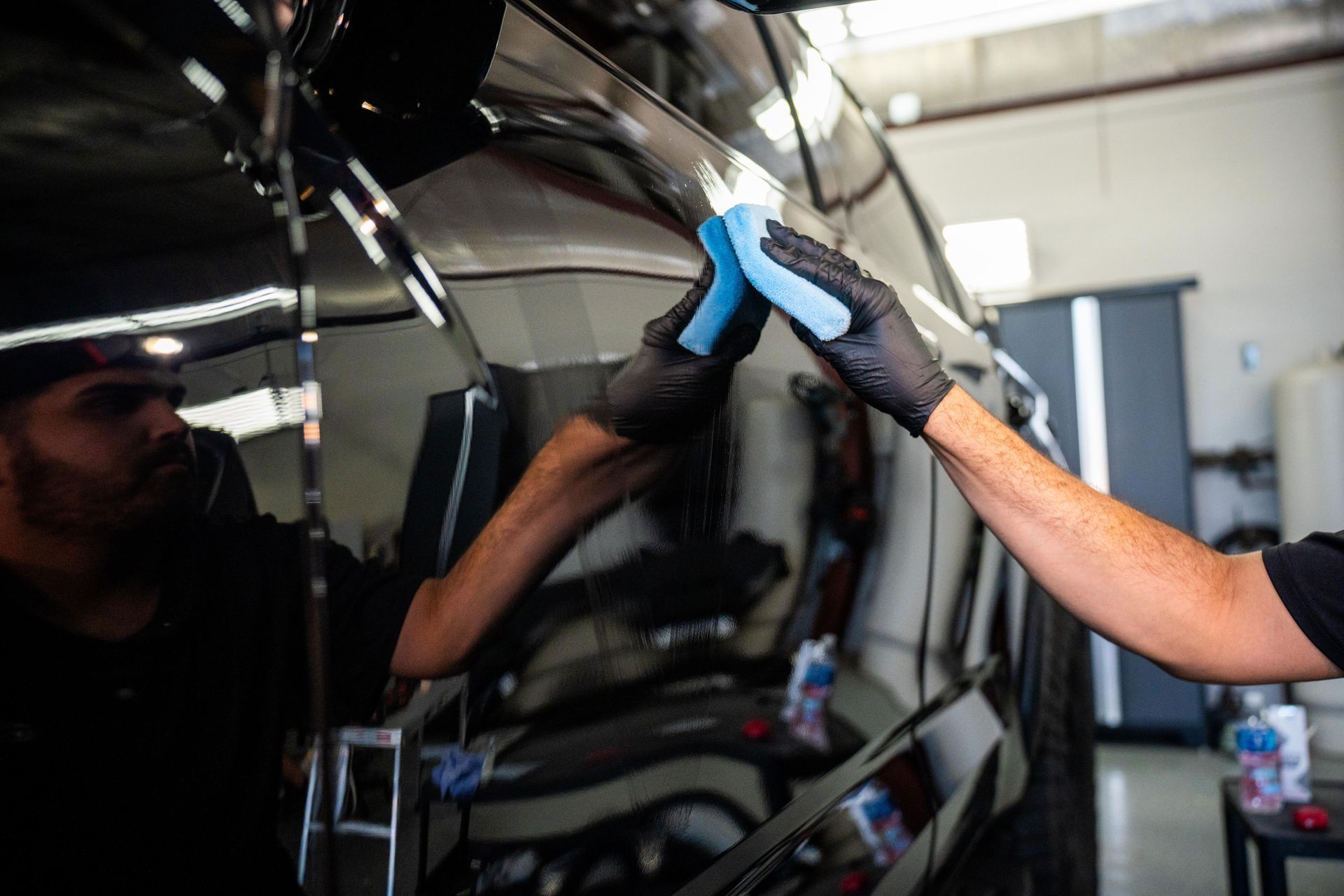 A man is cleaning a car with a cloth in a garage.