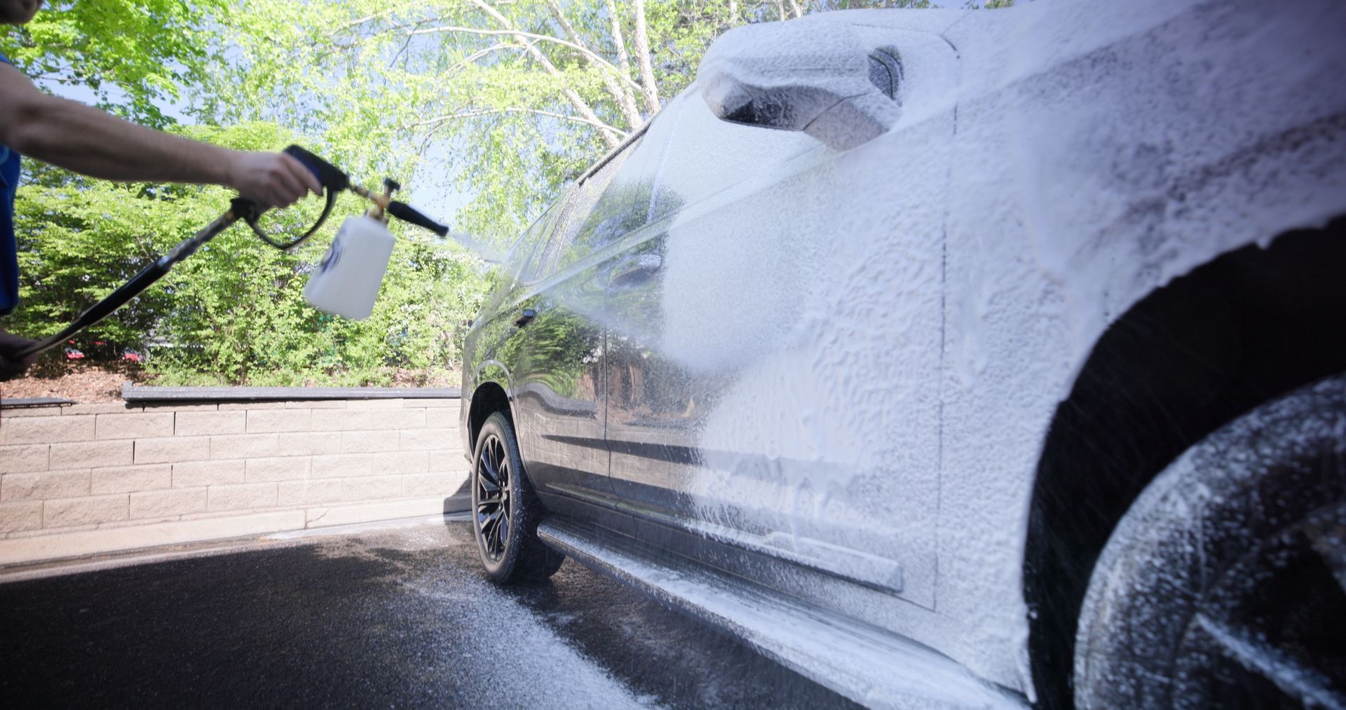 A man is washing a car with a high pressure washer.