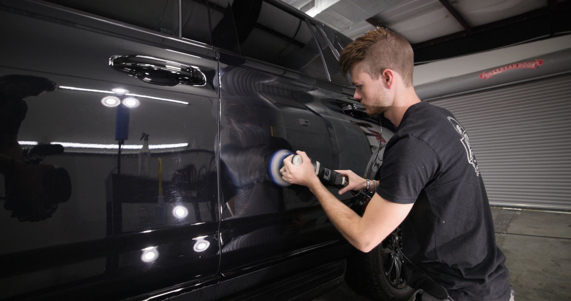 A man is polishing a black car in a garage.
