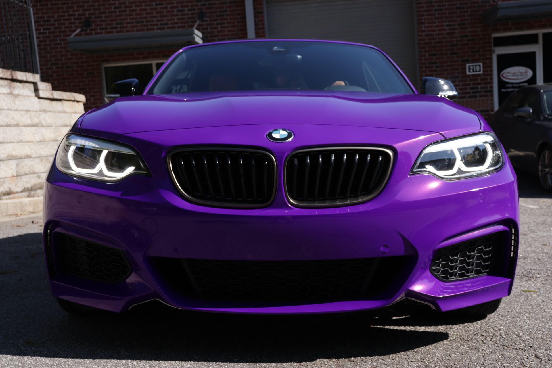 A purple bmw is parked in front of a brick building.