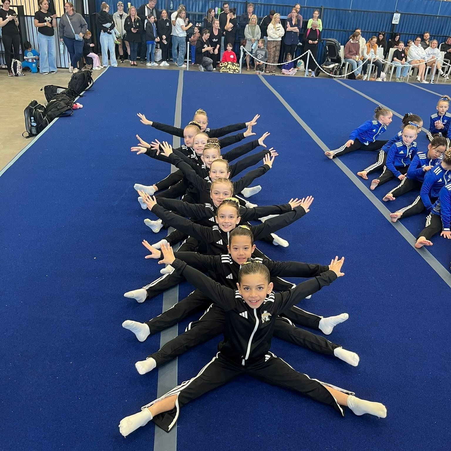 Gymnastics Team in Black Outfits Performs a Star-shaped Pose on a Blue Mat — Gold Medal Gymnastics In Molendinar, QLD