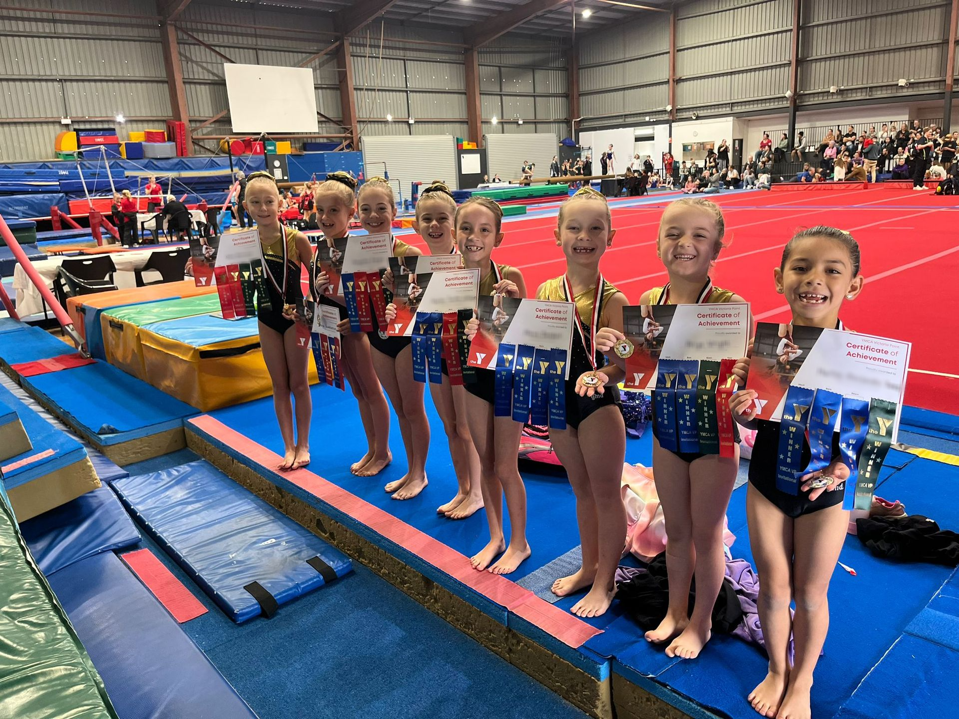 A Group Of Young Girls Are Standing On A Balance Beam In A Gym Holding Medals — Gold Medal Gymnastics In Molendinar, QLD