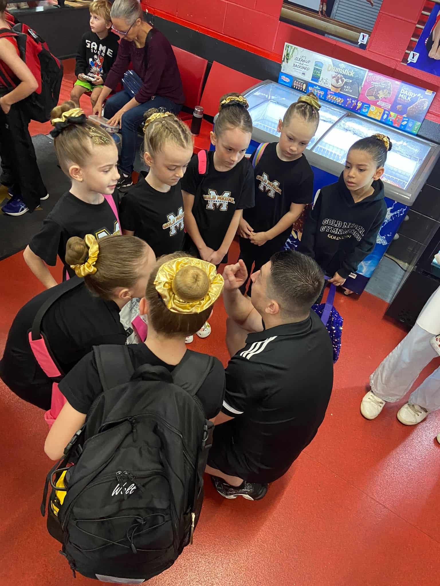 Young Girls Are Sitting In A Circle Around A Man — Gold Medal Gymnastics In Molendinar, QLD