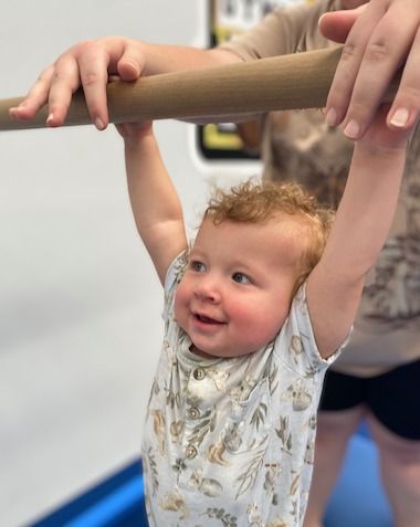 A Baby Is Hanging From A Bar And Smiling — Gold Medal Gymnastics In Gold Coast, QLD