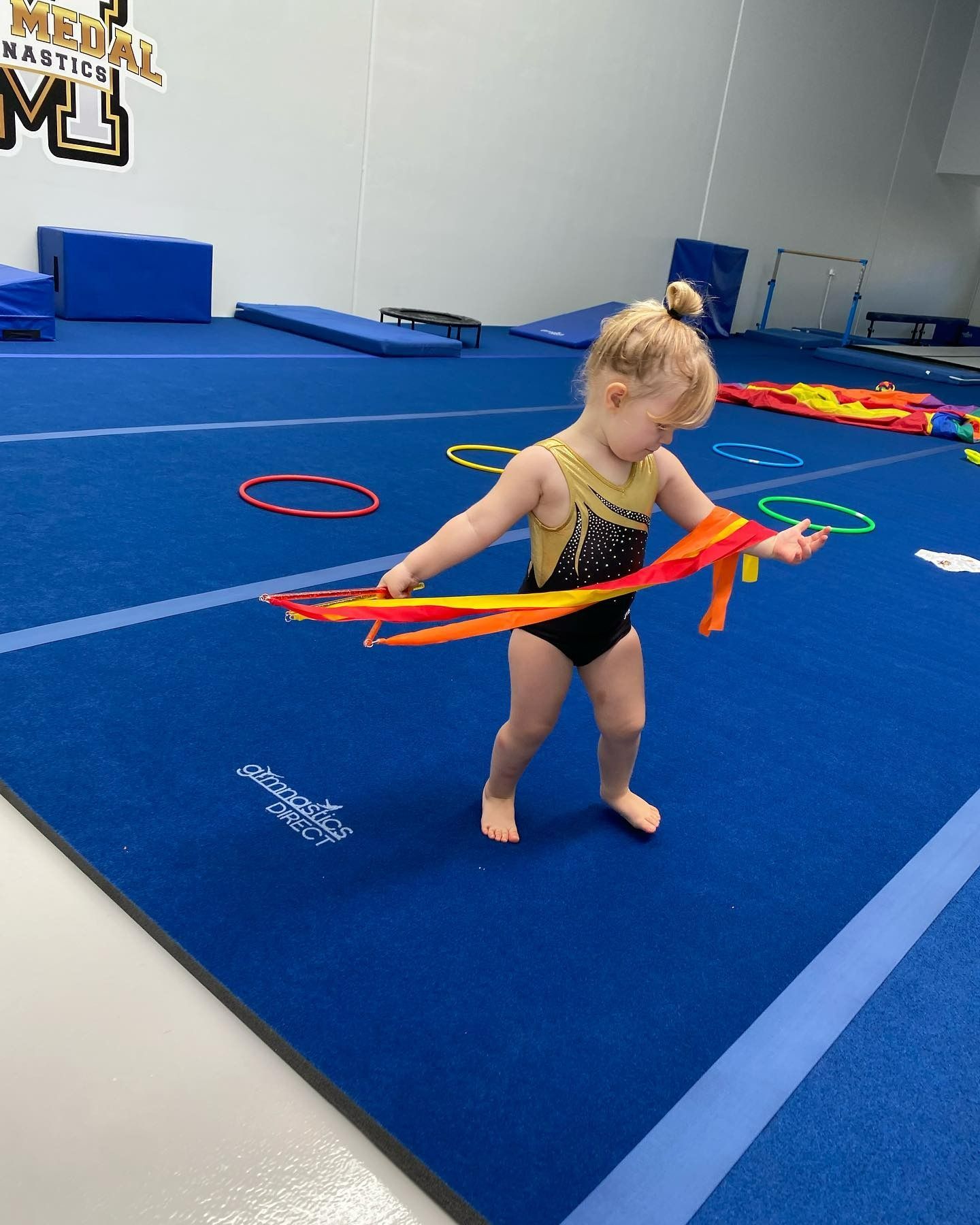 A Little Girl Is Playing With A Ribbon On A Gym Floor — Gold Medal Gymnastics In Molendinar, QLD