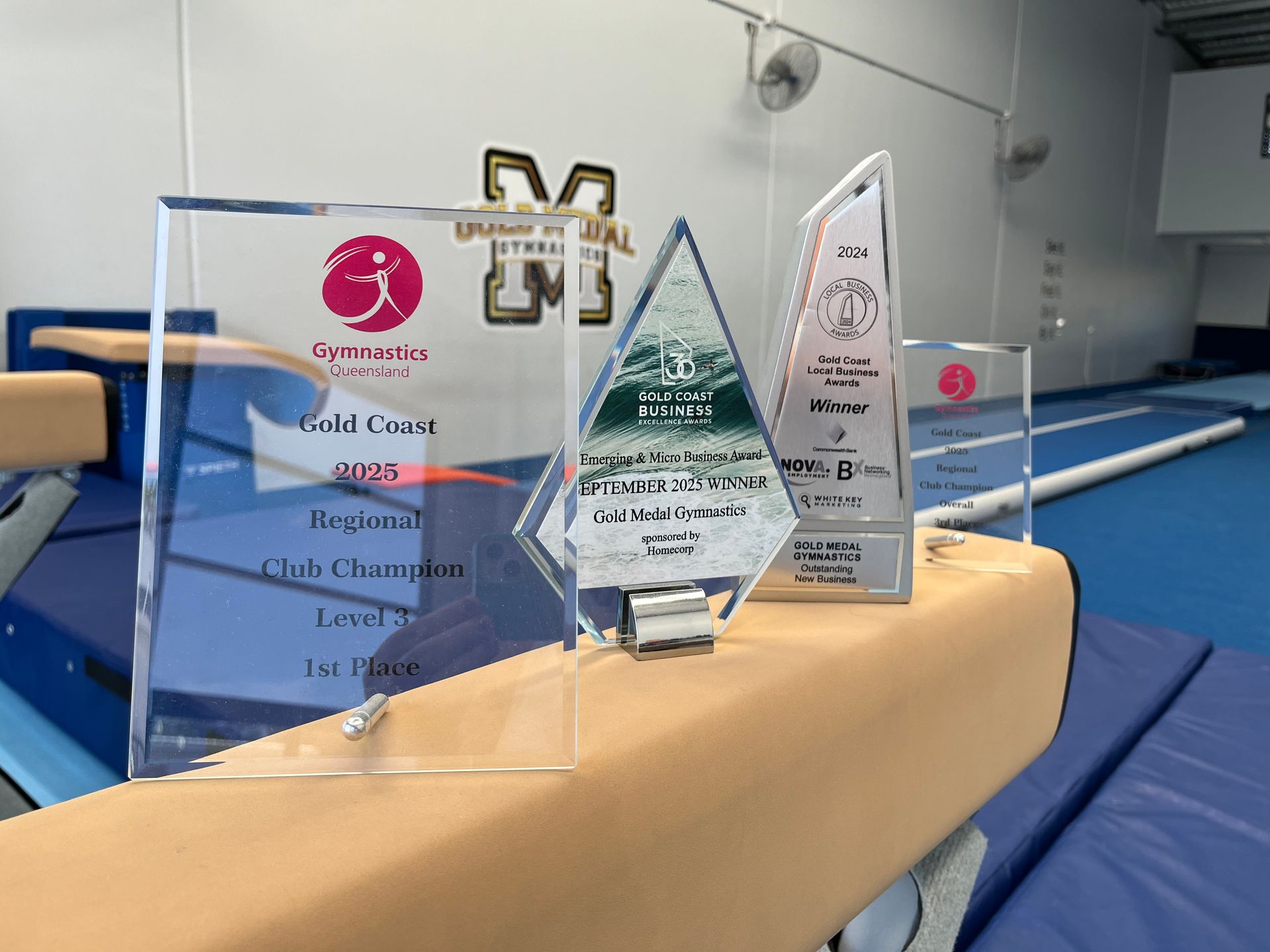 Trophies on balance beam in a gym; Regional Club Champion Level 7, 1st Place.