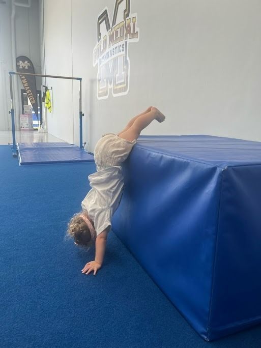A Little Girl Is Doing A Handstand On A Blue Mat — Gold Medal Gymnastics In Gold Coast, QLD