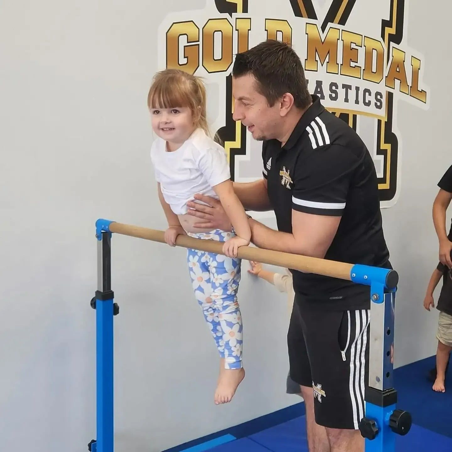 A Man Helps A Little Girl On A Bar — Gold Medal Gymnastics In Molendinar, QLD