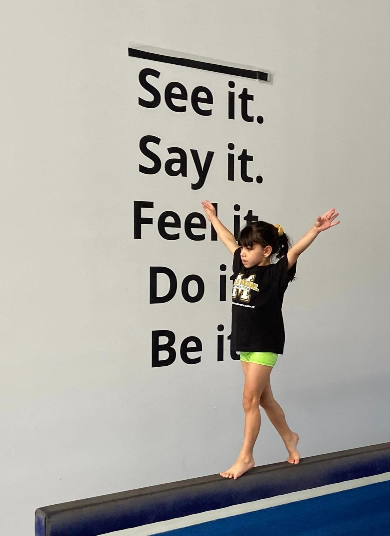 A Little Girl Balances On A Balance Beam In Front Of A Wall — Gold Medal Gymnastics In Gold Coast, QLD