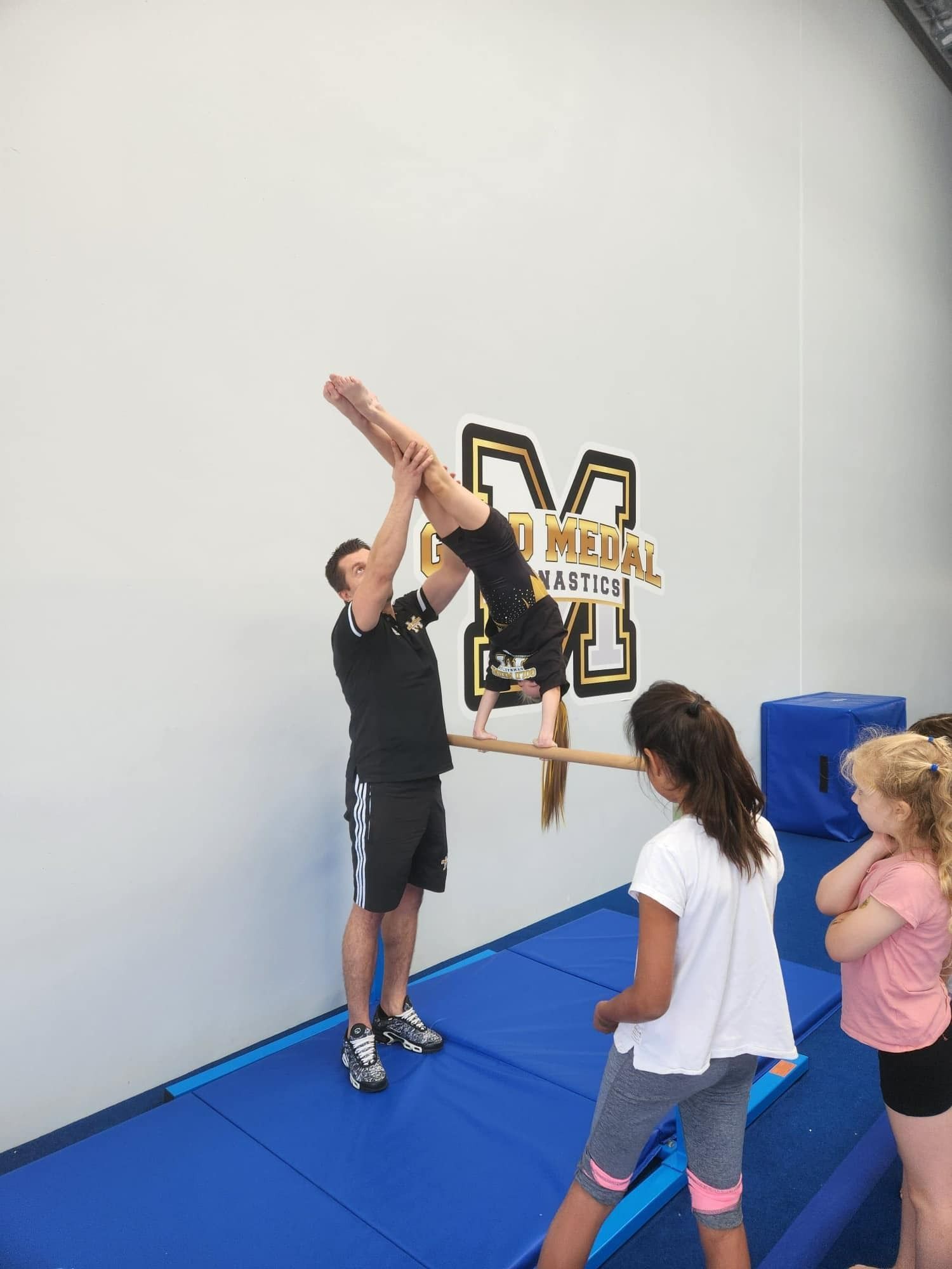 A Man Is Helping A Girl Do A Handstand On A Bar In A Gym — Gold Medal Gymnastics In Molendinar, QLD