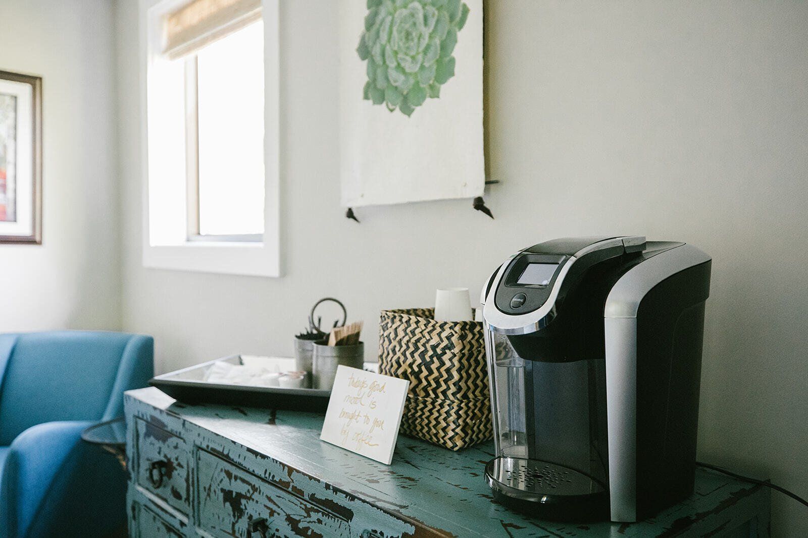 A coffee maker is sitting on top of a blue dresser in a living room.